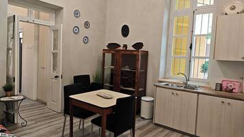 A compact kitchen with a dining table, chairs, a cabinet, and a window with yellow shutters.