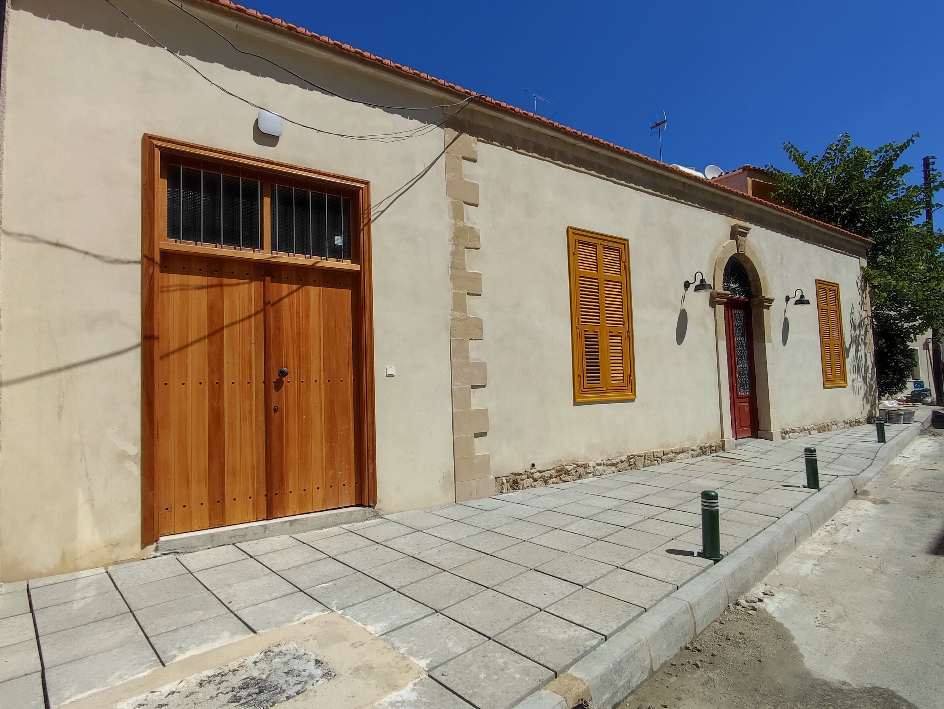 A building with a large wooden door, a window with shutters, and a tiled walkway.
