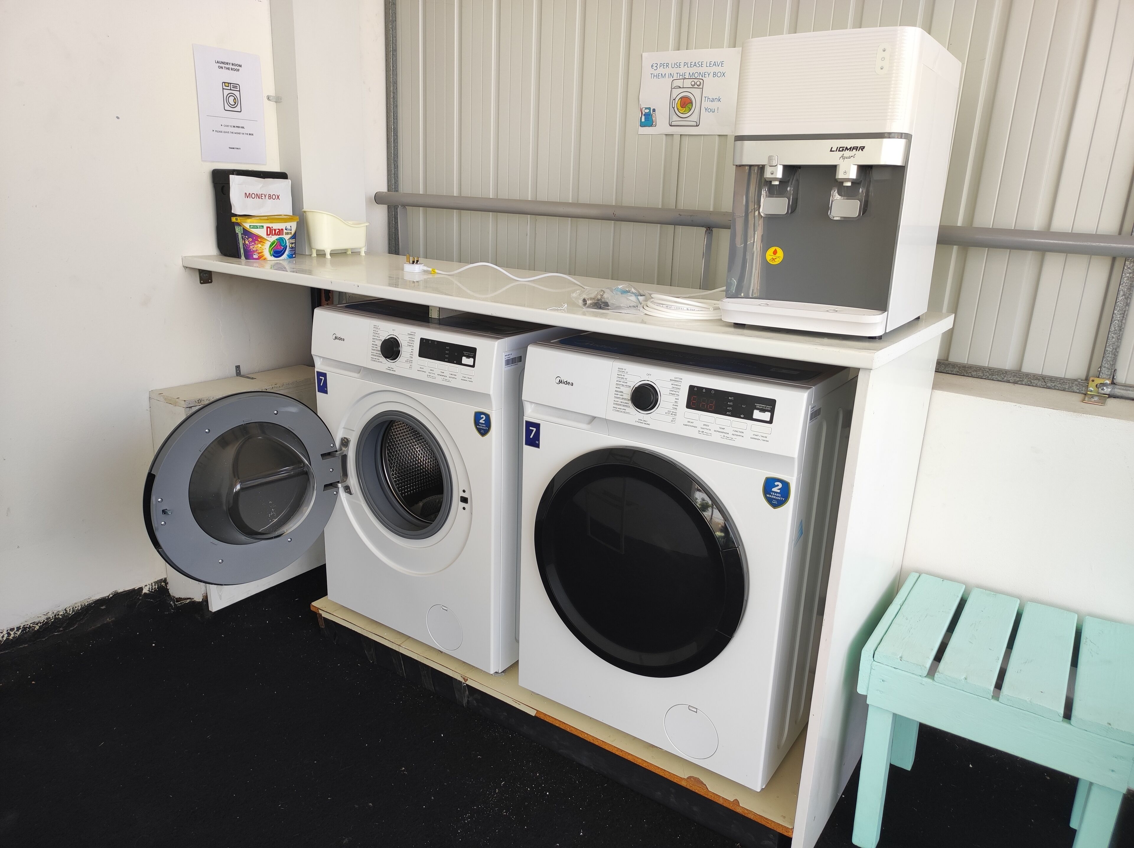 A laundry area with two washing machines, a water dispenser, and a money box.