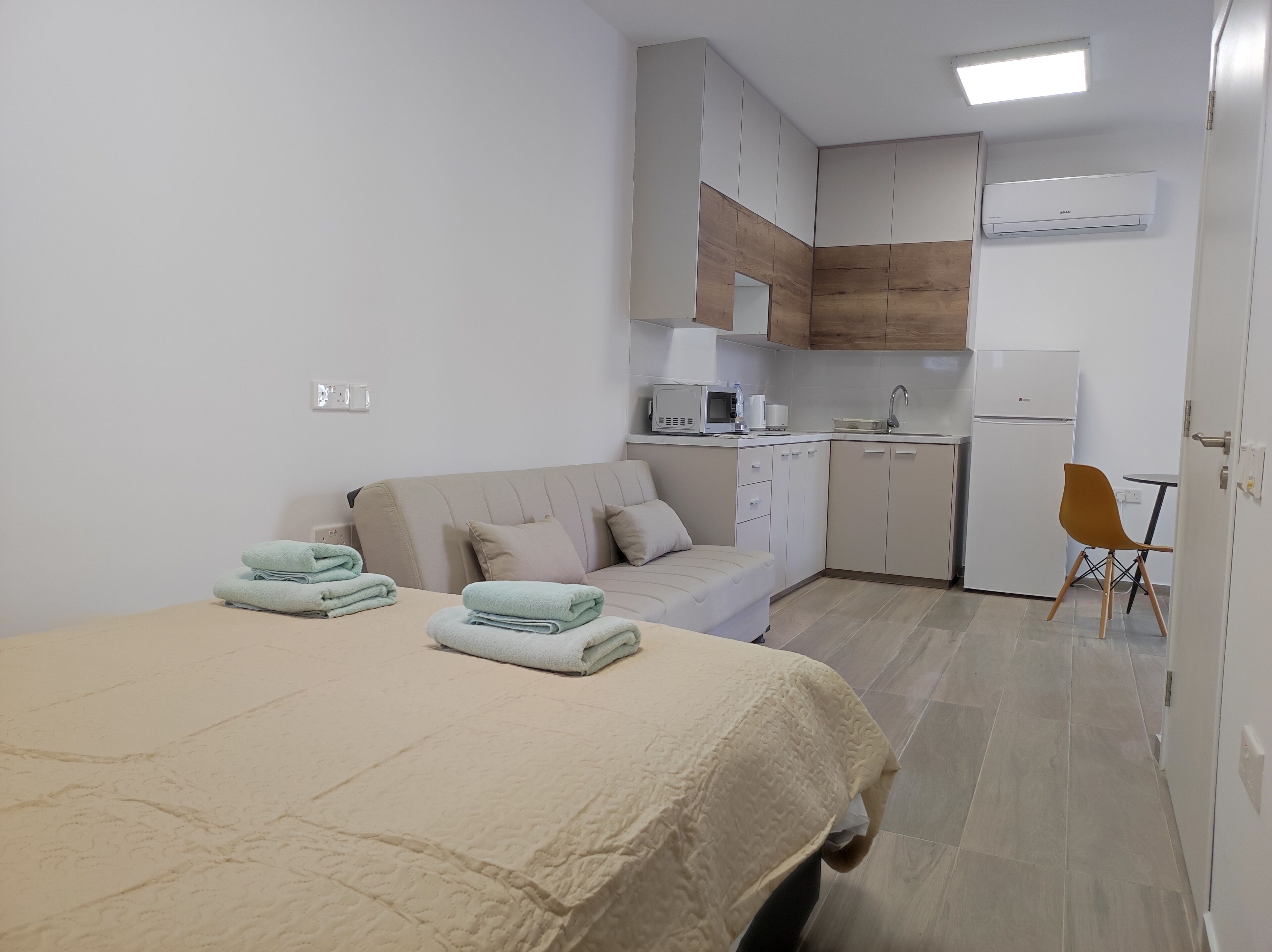 A compact hotel room with a bed, a sofa, a kitchenette, and a small dining area.