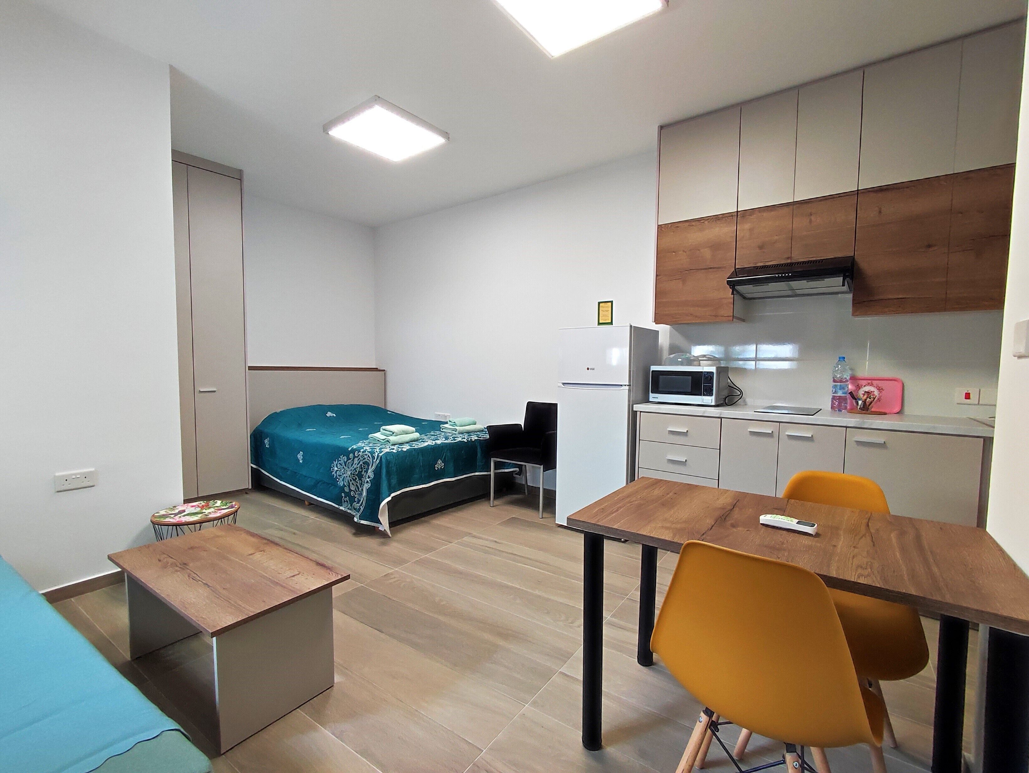 A compact room with a bed, a desk, a chair, a microwave, and a kitchenette.