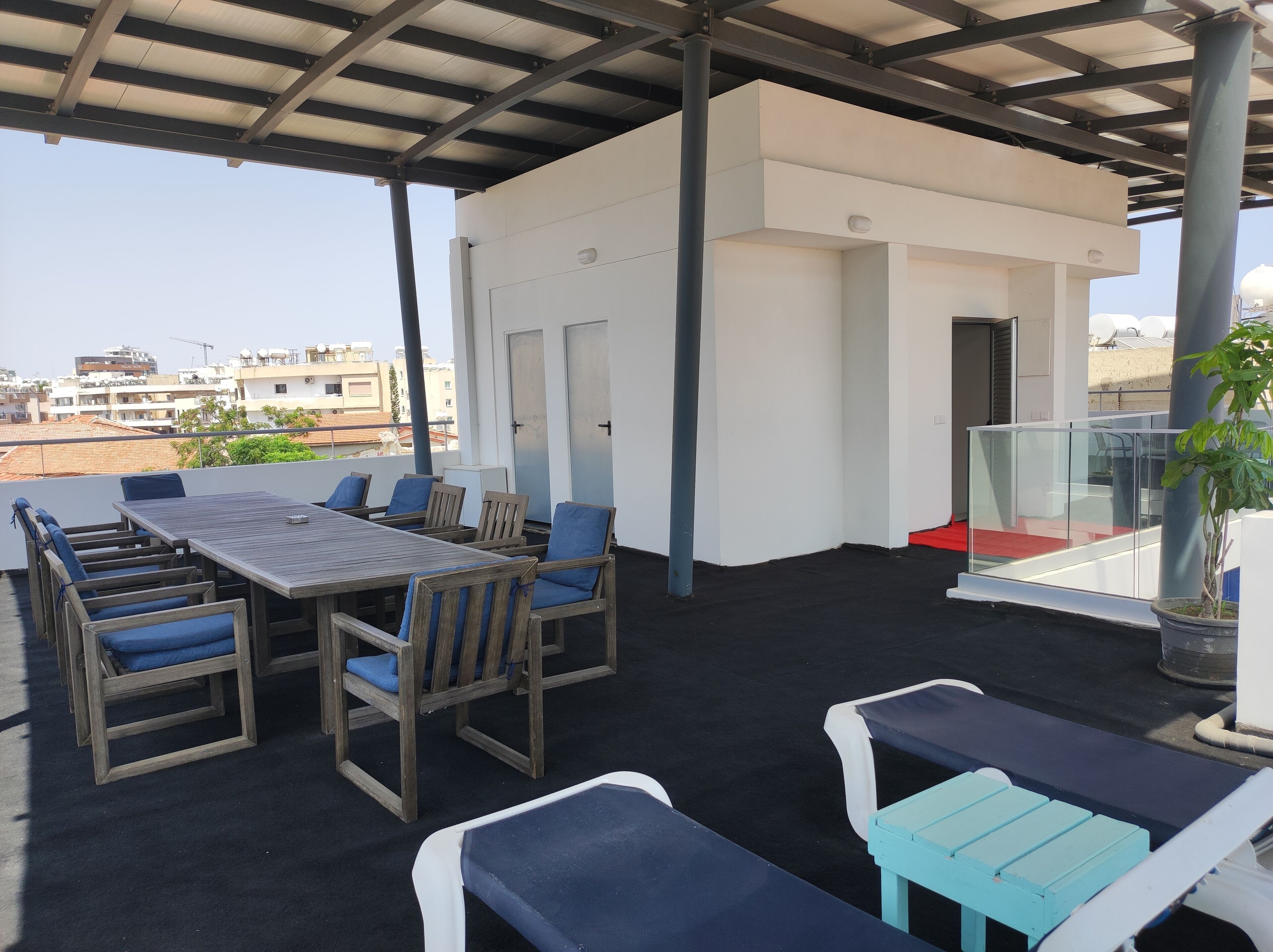 An outdoor patio with a wooden table and chairs, a small white building, and a view of the cityscape.
