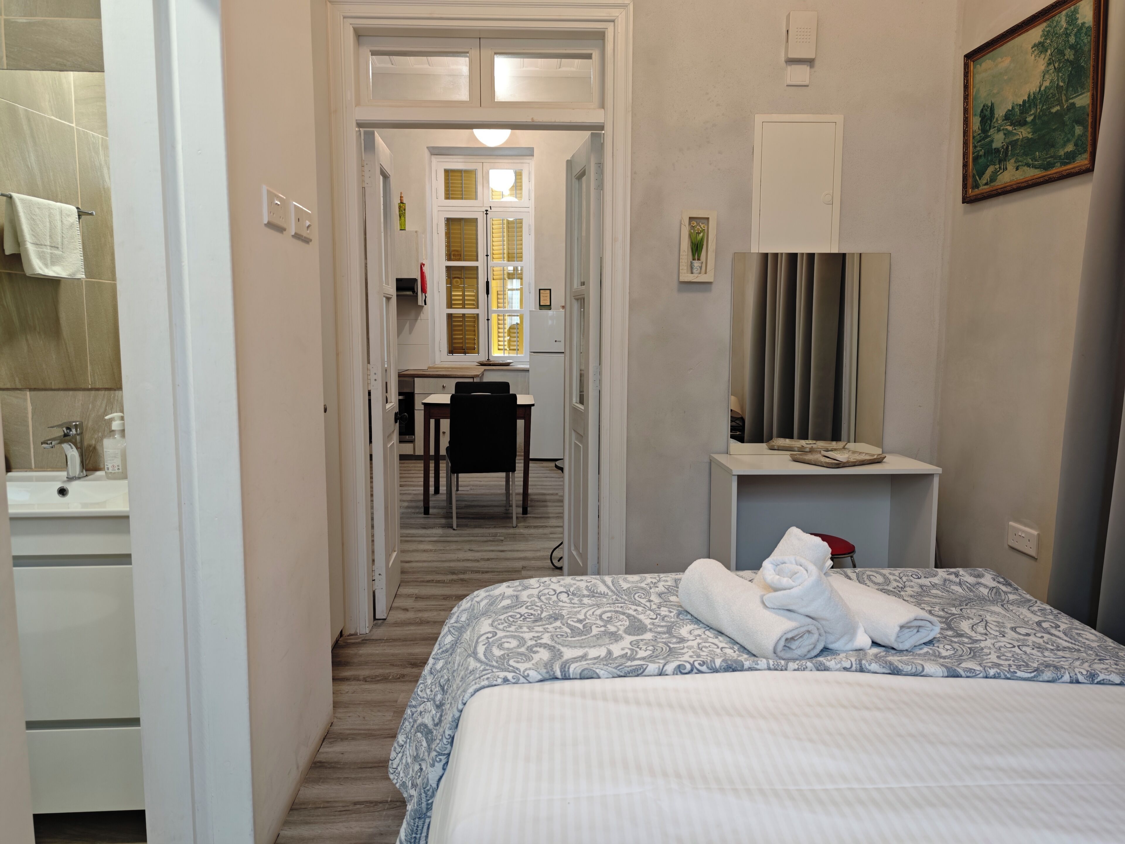 A hotel room with a bed, a desk, a chair, a bathroom with a sink, and a mirror.