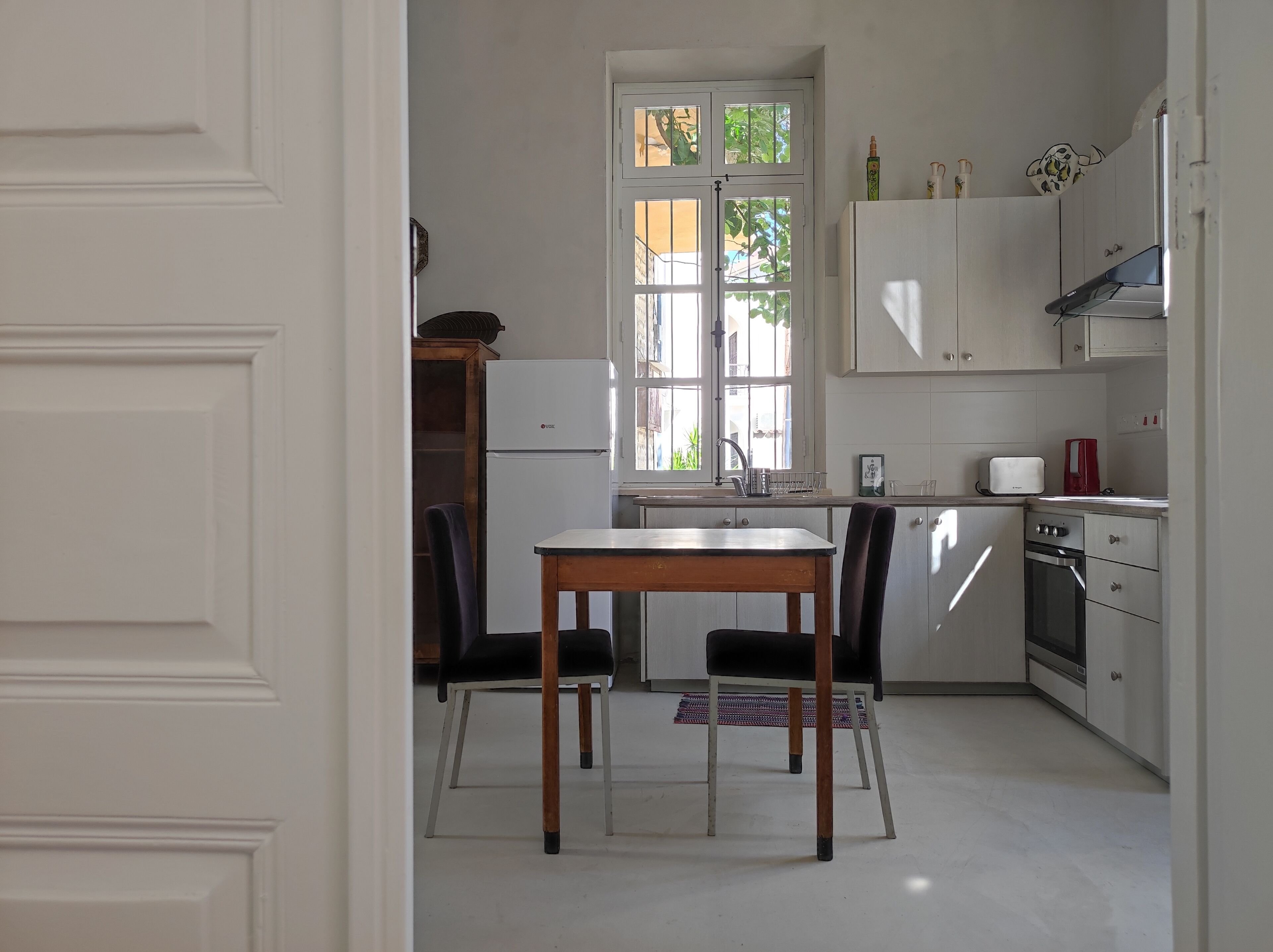 A compact kitchen with white cabinets, a built-in oven, and a window with a view of greenery outside.