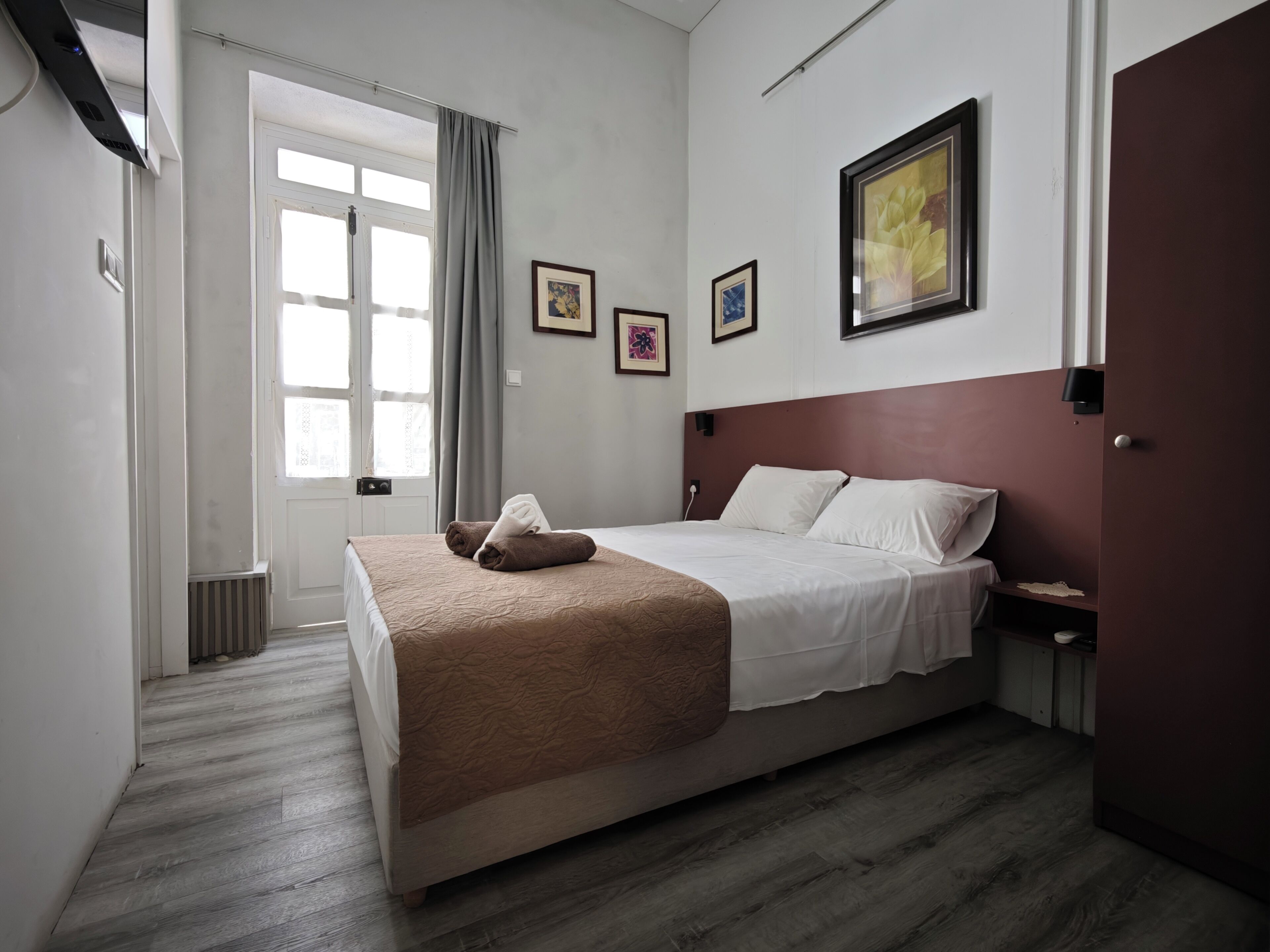 A hotel room with a bed, a window with curtains, a wall-mounted picture, and a door.