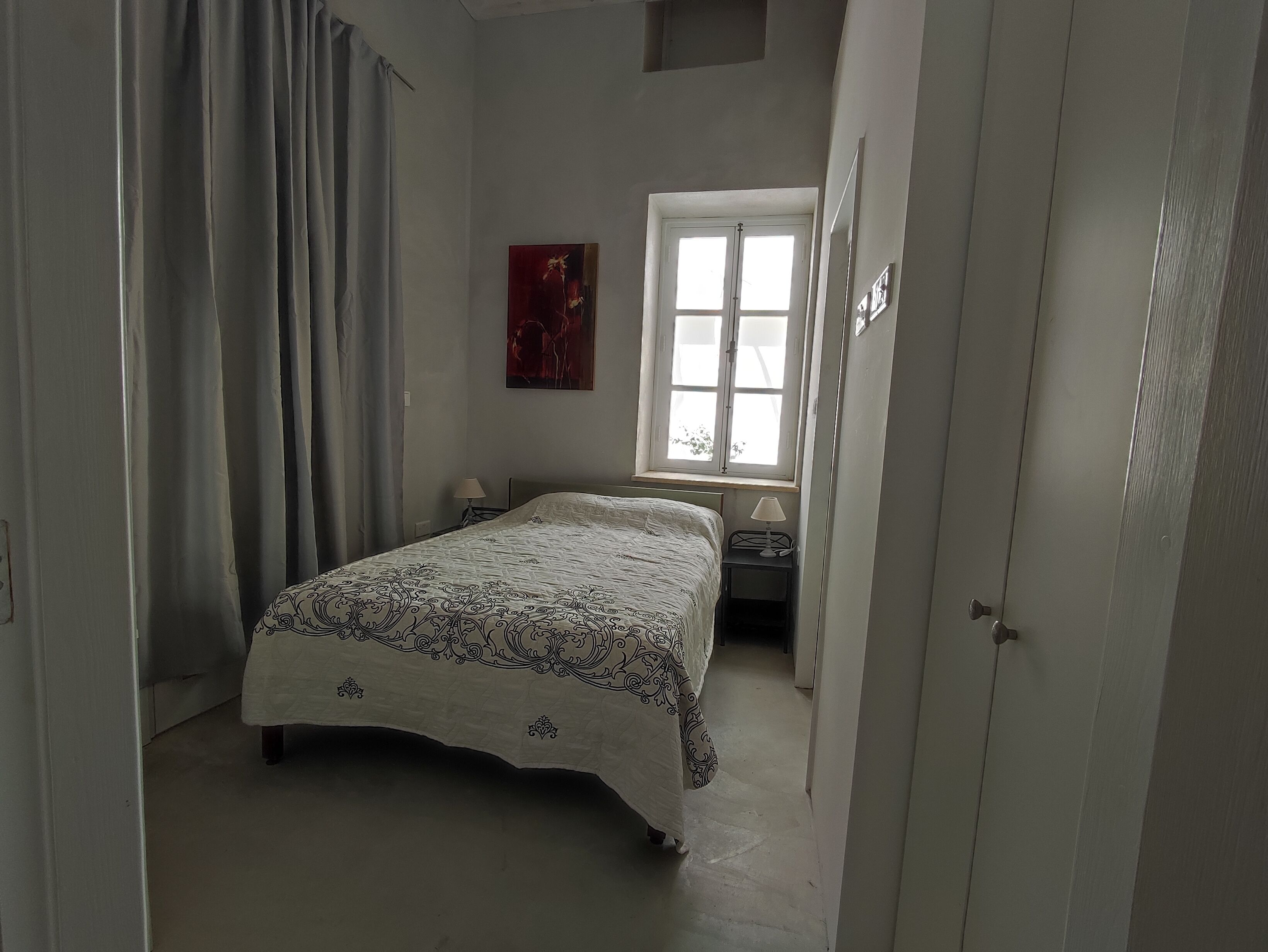 Ein Schlafzimmer mit Bett, Fenster, Nachttisch und einem Gemälde an der Wand.