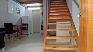 Una escala que condueix a un pis superior, una zona de menjador amb taula i cadires, i una cuina equipada.