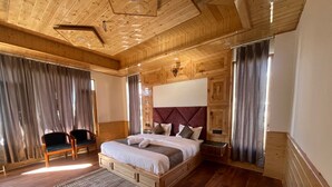 A wooden-paneled bedroom with a large bed, a nightstand, a chair, and a window with curtains. - Hotel Mountain Blue Manali (Manali)