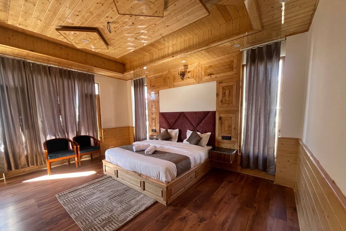 Ein Schlafzimmer mit Holzwandverkleidung, einem großen Bett, einem Nachttisch, einem Sessel und einem Fenster mit Vorhängen.