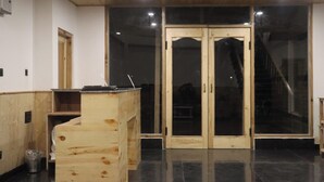 A room with a wooden reception desk, a black tiled floor, and a set of double doors leading to another area. - Hotel Mountain Blue Manali (Manali)