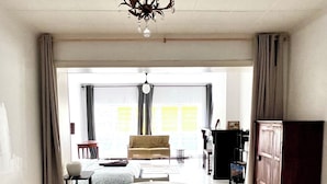 A spacious room with a round dining table, white chairs, a chandelier, and a large window with curtains. - Studio à 800 m de la Grand Place (Brussels)