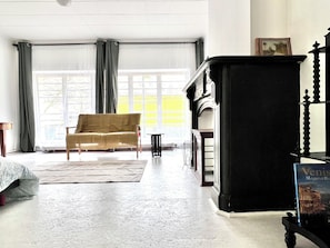 Een kamer met een bank, een open haard en een groot raam met gordijnen.