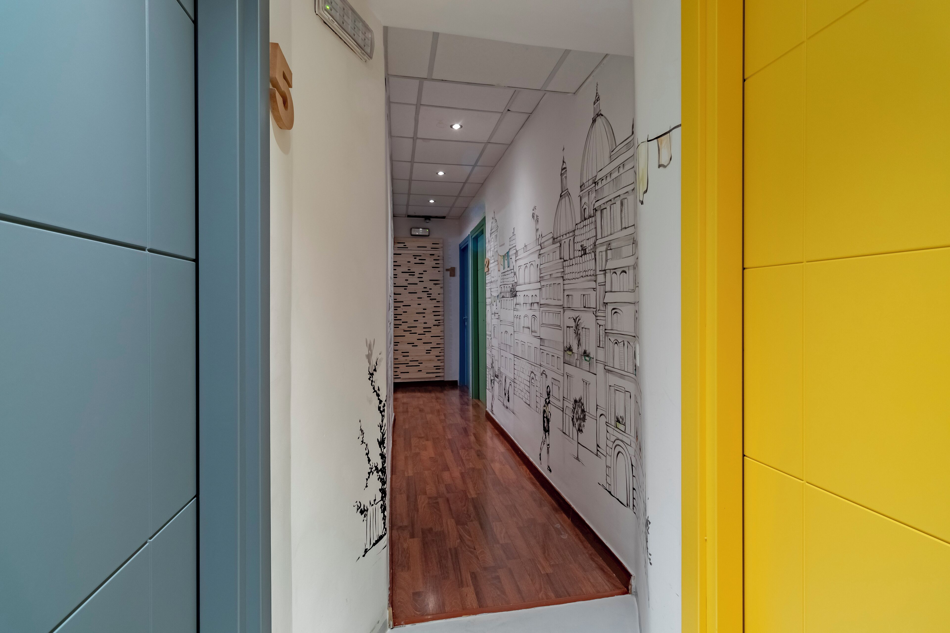 A hallway with wooden flooring, blue and yellow walls, and a mural of architectural drawings.
