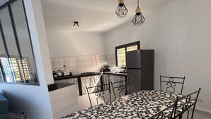 A modern kitchen with a dining table, chairs, and hanging lights. - Villa Kalélou (Nianing)