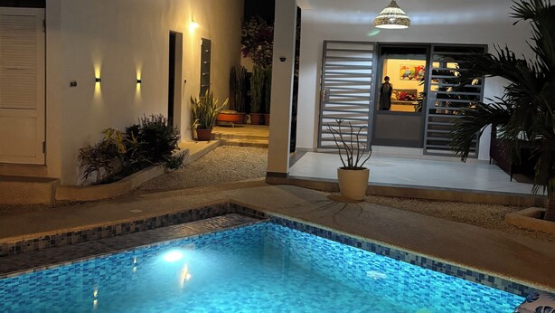 A modern pool area with a clear blue pool, surrounded by a white building with a sliding glass door. - Villa Kalélou (Nianing)