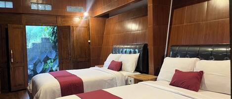 A hotel room with two beds, wooden paneling, and a view of a garden through a door.
