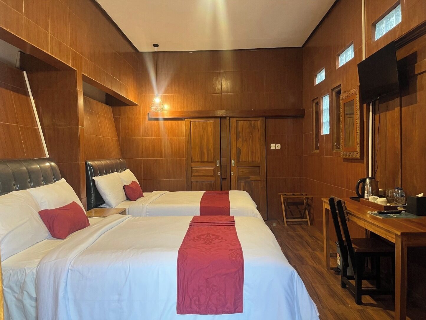 A hotel room with two beds, wooden walls, a desk with a chair, and a large mirror.