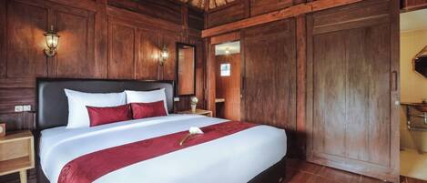 A large bed with white and red bedding, wooden walls, and a woven ceiling.