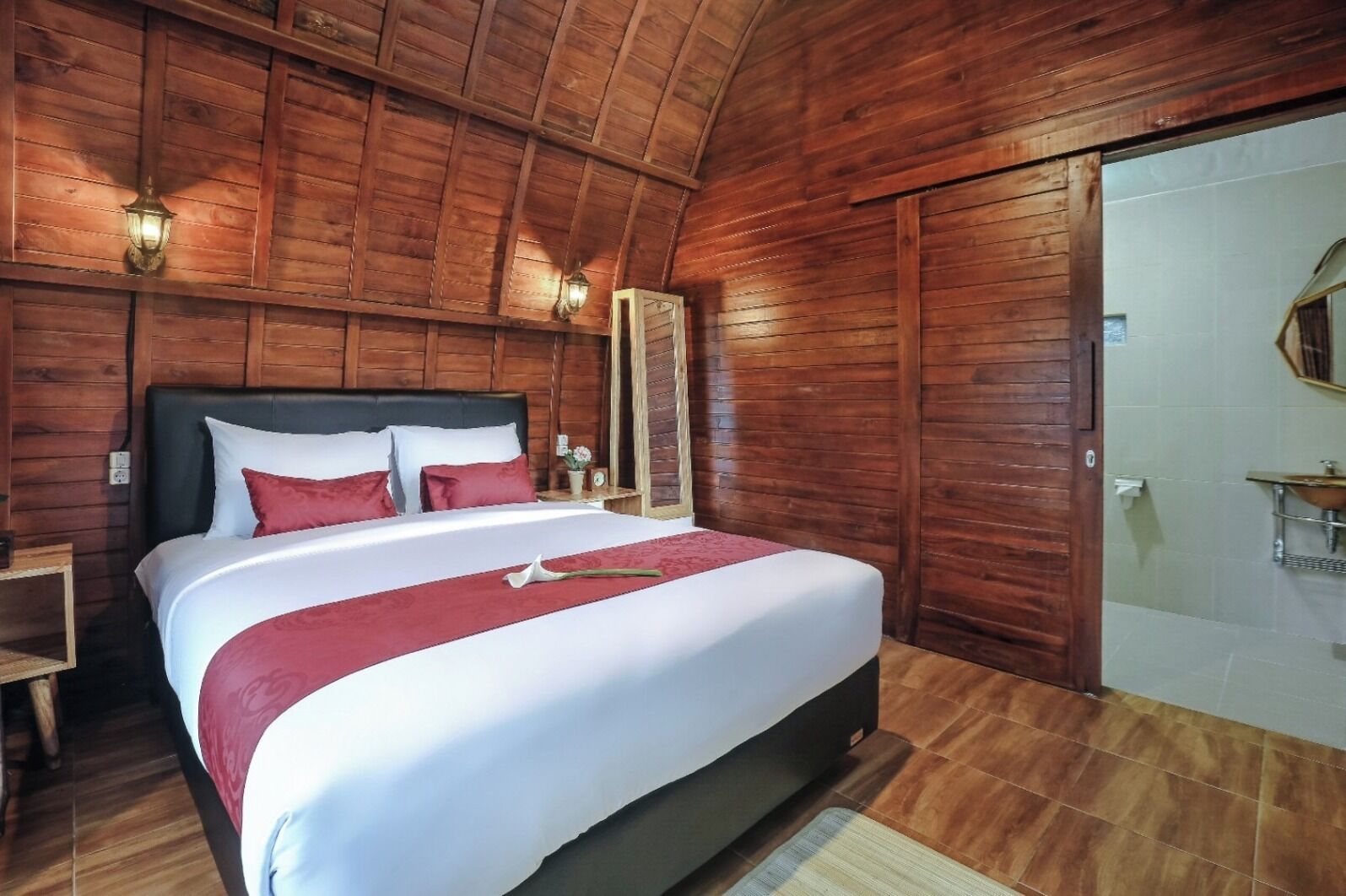Une chambre à coucher aux murs lambrissés, avec un grand lit, deux tables de chevet et une salle de bain équipée d’un lavabo et d’un miroir.