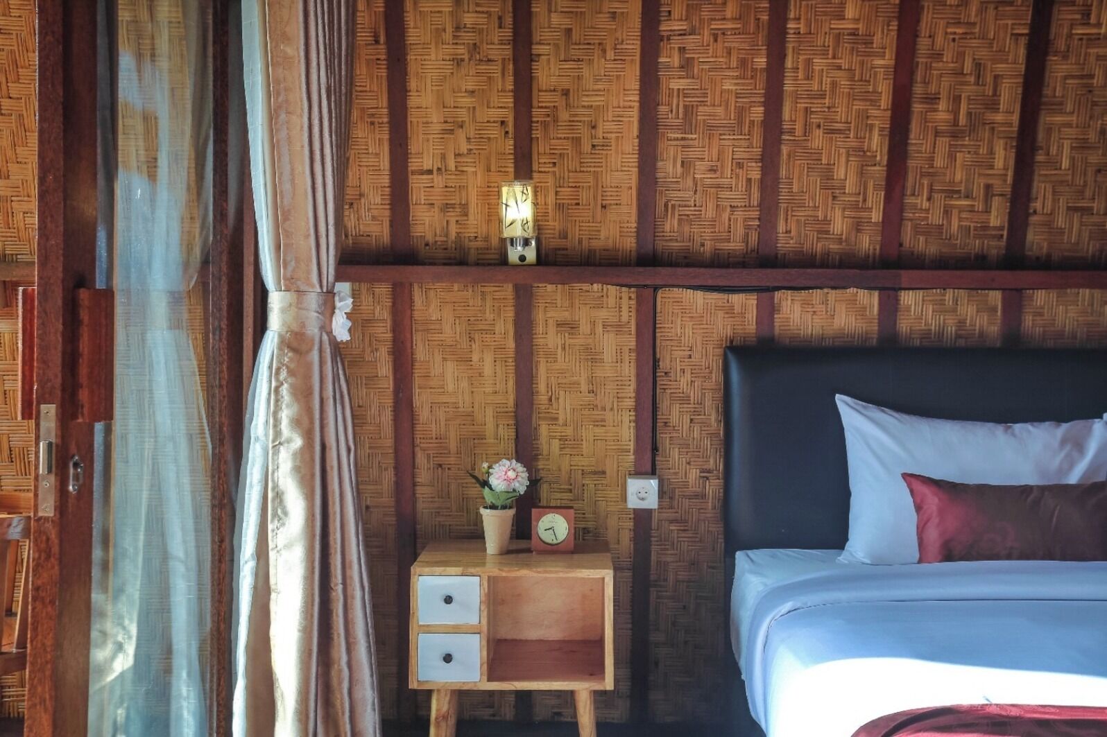 A room with a bed, a nightstand with a clock, and a wall with a woven pattern.