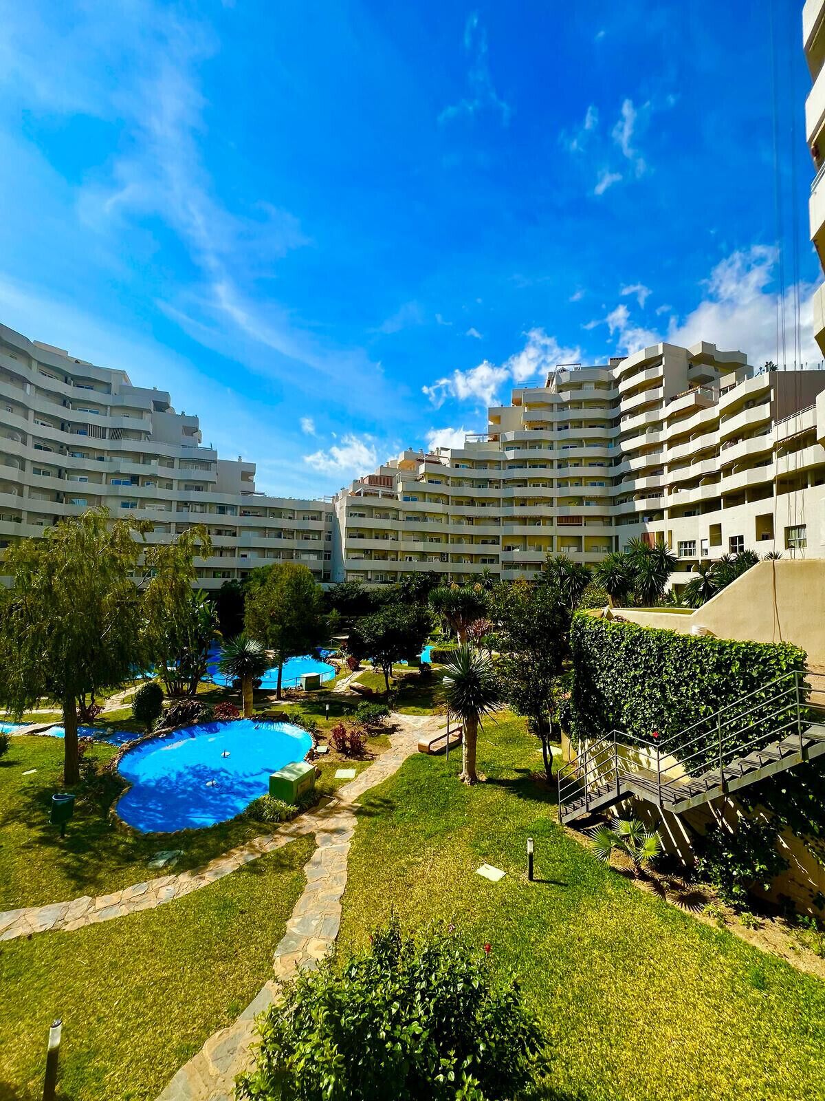 Un hotel con varios pisos, piscinas al aire libre y jardines bien cuidados.