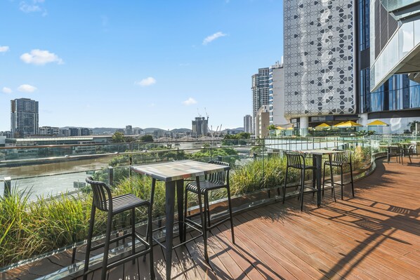 A rooftop terrace with outdoor seating, a view of a river, and modern buildings in the background.