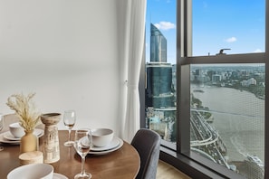 A dining area with a table set for two, a view of a cityscape through large windows, and a modern building with a 'super' sign.