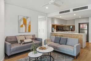 Una sala de estar moderna con un sofá gris, una mesa de centro y un comedor, con una cocina al fondo.