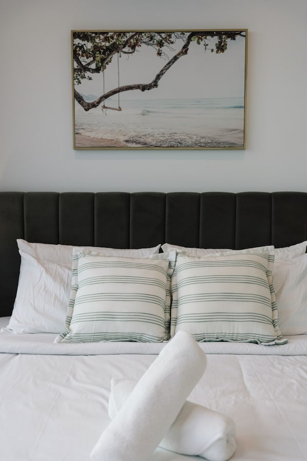 A bed with white bedding and striped pillows, a dark headboard, and a framed picture of a beach scene on the wall.