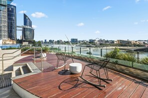 A wooden deck with outdoor seating, overlooking a river and city skyline.