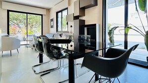 A modern dining area with a glass table, black chairs, and a large window offering a view of trees and a building. - The Flexrent Port - Abyssinia (Riccione)