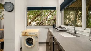 Eine moderne Küche mit eingebauter Waschmaschine und Trockner, einem Edelstahlspülbecken und einem Fenster mit Blick auf Bäume.