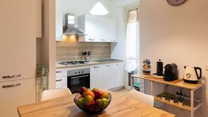 Una cocina moderna con armarios blancos, una encimera de madera, una estufa a gas y un lavabo. Hay un cuenco con fruta en la mesa y un hervidor sobre la encimera.