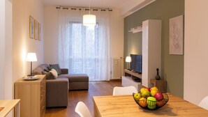 Una sala de estar moderna con un sofá, una mesa de comedor con frutero y un televisor.