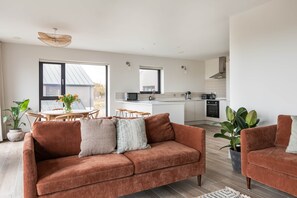 A modern living room with a sofa, a dining table, and a kitchen in the background.