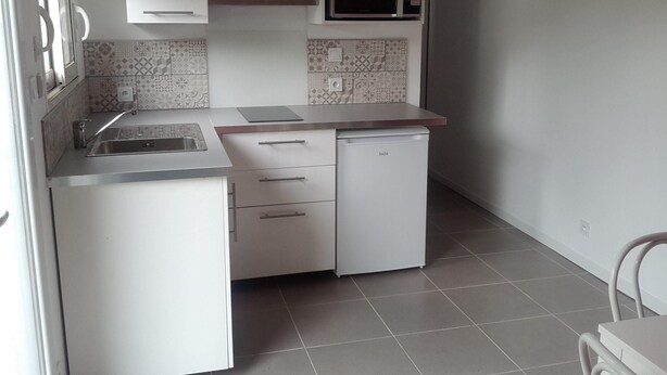 Una cocina pequeña con armarios blancos, microondas integrado, un lavabo y un refrigerador compacto.