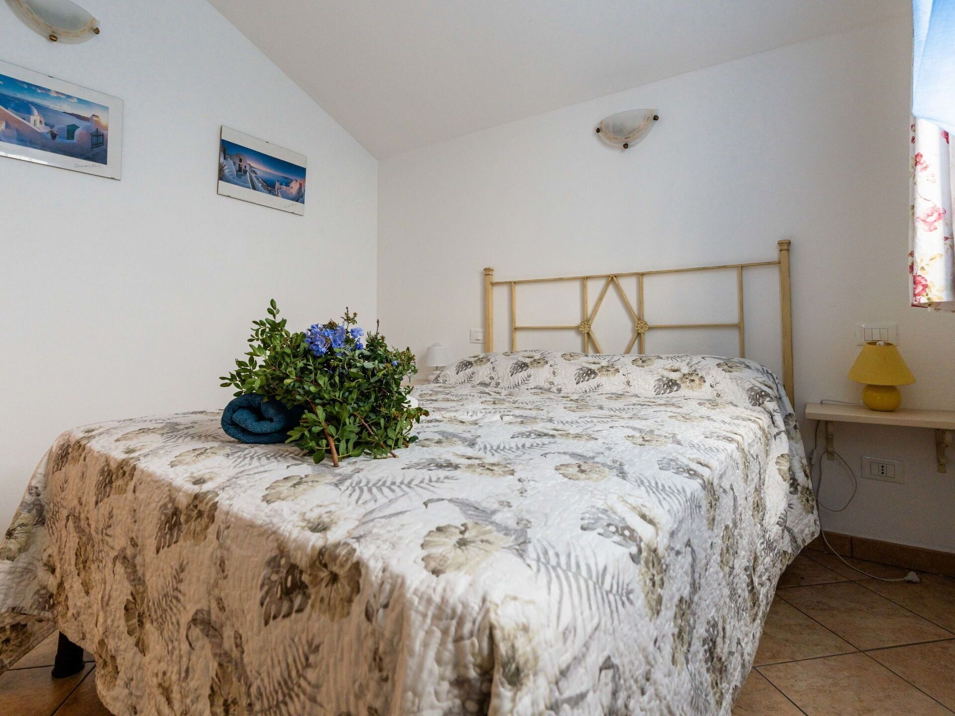 A bedroom with a bed, a small table with a lamp, and two framed pictures on the wall.
