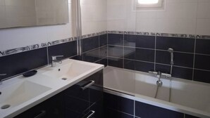 A bathroom with a white sink, a mirror, a bathtub, and black and white tiled walls. - Chez Malya, quiet house near the lake (Charavines)