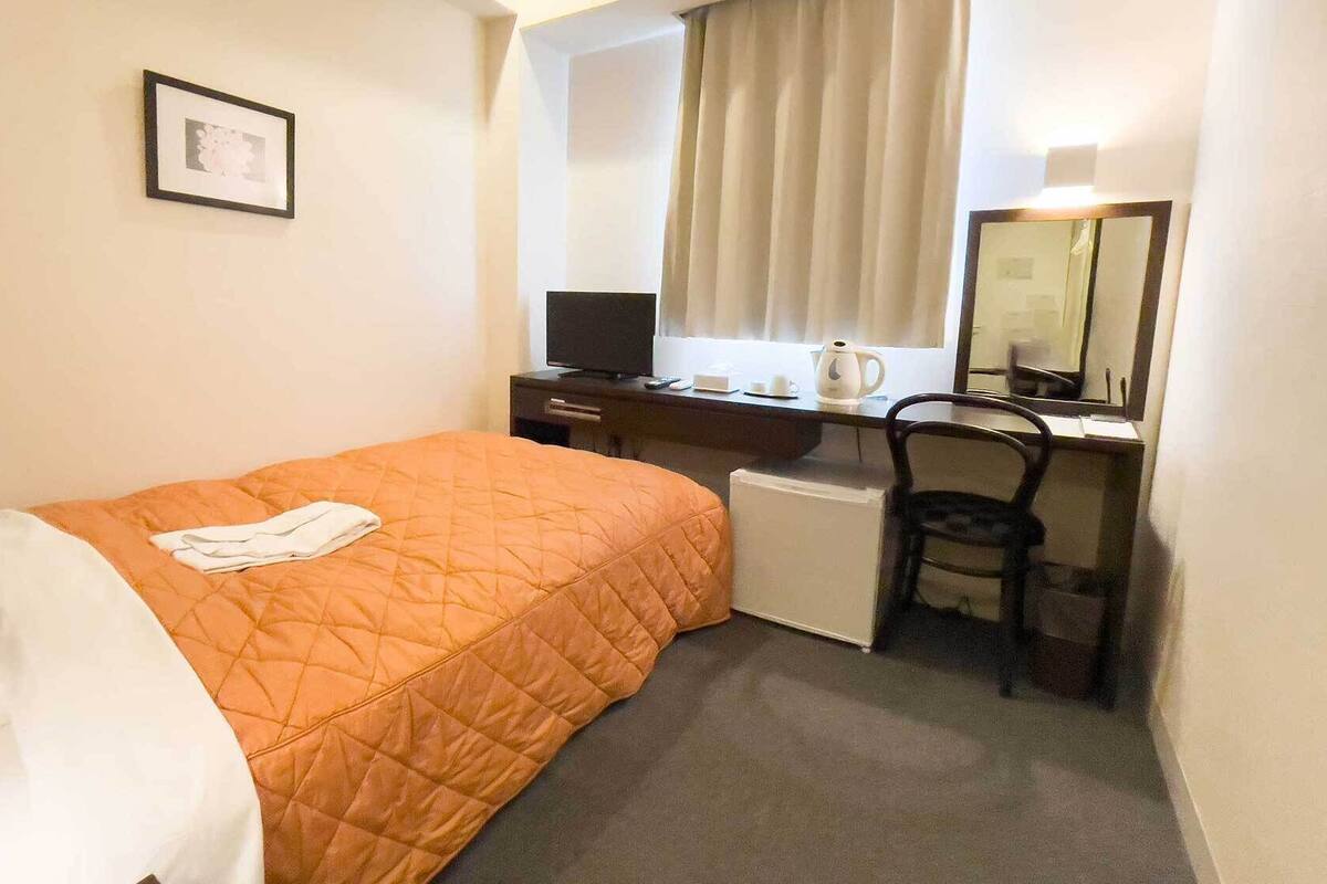 Una habitación de hotel con cama, escritorio, silla, televisor y espejo.