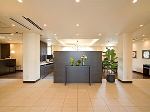 Un hall d’hôtel moderne avec un comptoir d’accueil, un espace salon et une grande plante en pot.