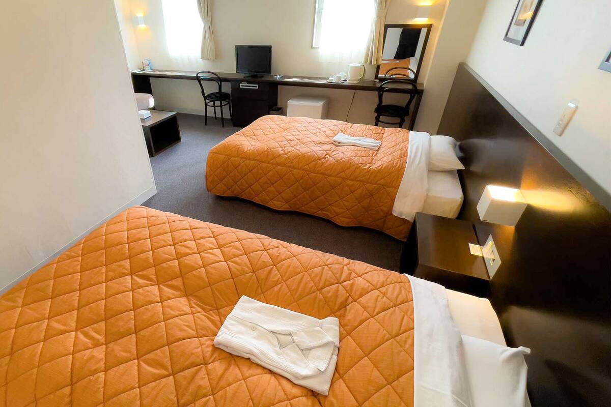 Una habitación de hotel con dos camas, un escritorio, una silla y un televisor.
