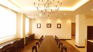 Ein Konferenzraum mit langem Tisch, Stühlen, einer Kristallleuchtreiter, gerahmten Bildern an der Wand und einem Fenster, das für natürliches Licht sorgt.