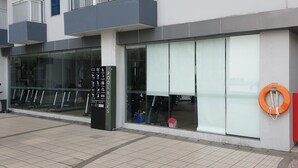 A modern building with large glass windows, a black sign with emergency instructions, and a red fire extinguisher mounted on the wall. - Cosmy Benson 38 Apartment (Surabaya)