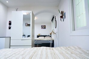 A bedroom with a bed, a dresser, a mirror, a window, and a door leading to another room. - moneystay deagu (Daegu)