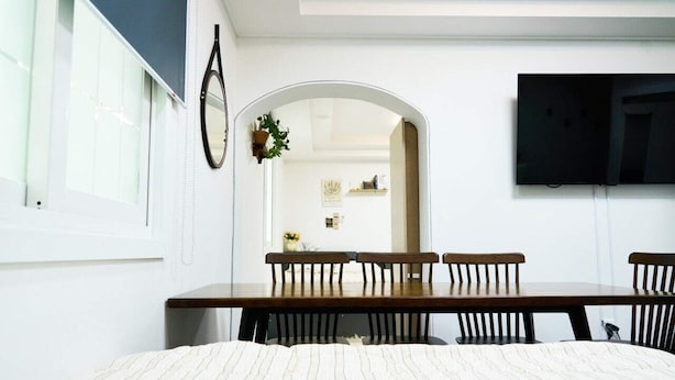 A bedroom with a bed, a wooden dining table with chairs, a TV mounted on the wall, and a mirror. - moneystay deagu (Daegu)