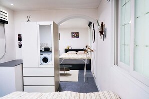 A compact bedroom with a bed, a small table, a washing machine, and a window. - moneystay deagu (Daegu)