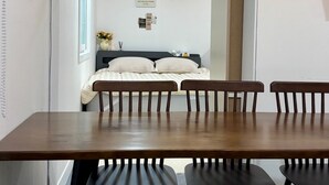 A dining area with a wooden table and four chairs, a mirror on the wall, and a view into a bedroom with a bed and a shelf. - moneystay deagu (Daegu)
