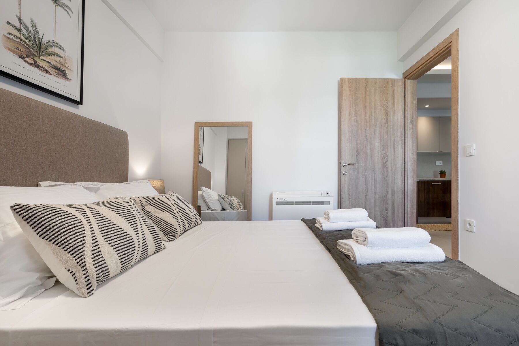 A modern hotel room with a large bed, a bedside table, a mirror, a wardrobe, and a wall-mounted air conditioner.