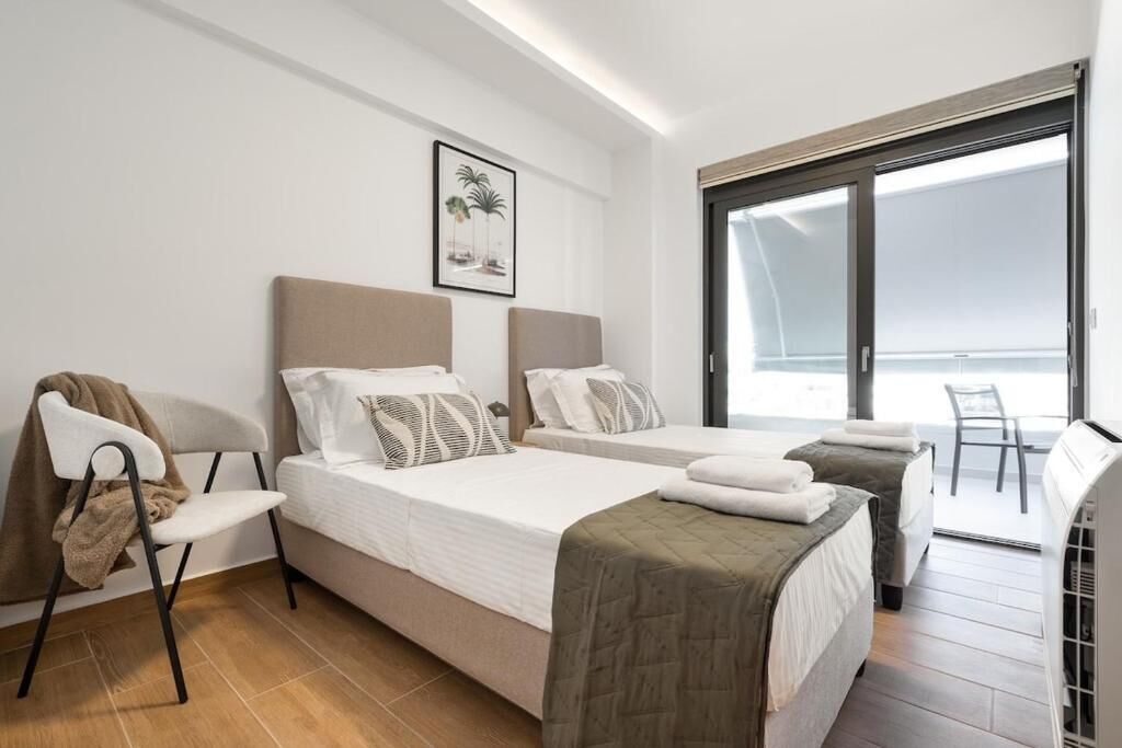 A hotel room with two beds, a chair, a large window, and a door leading to a balcony.