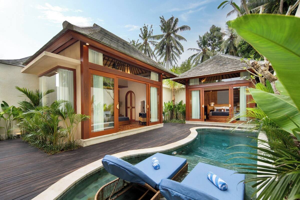 A resort with a swimming pool, wooden deck, and tropical plants.